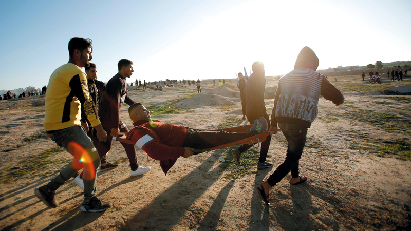 فلسطينيون يحملون جريحاً أصيب في مواجهات مع قوات الاحتلال على حدود غزة . أ.ف.ب