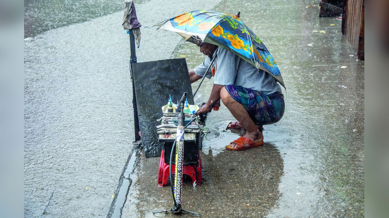 سائق عربة يحمل مظلة أثناء عمله خلال يوم ممطر. إي.بي.إيه