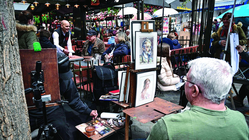 A man poses for a portrait of a painter at Place du Tertre, the famous painters' square in Montmartre, northern Paris, on April 25, 2024. On the Place du Tertre, artists but there is no rush of tourists and the restaurant terraces are rather empty, just a few days before the 2024 Paris Olympics Games. (Photo by Miguel MEDINA / AFP)