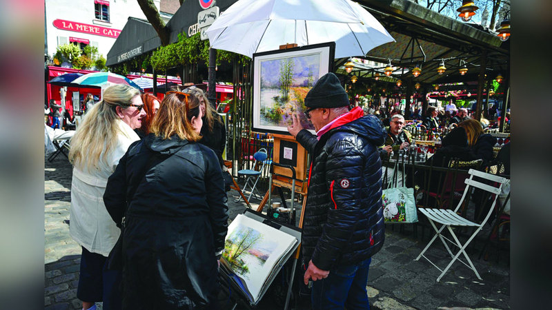 A painter shows his art work to tourists at Place du Tertre, the famous painters' square in Montmartre, northern Paris, on April 25, 2024. On the Place du Tertre, artists but there is no rush of tourists and the restaurant terraces are rather empty, just a few days before the 2024 Paris Olympics Games. (Photo by Miguel MEDINA / AFP)