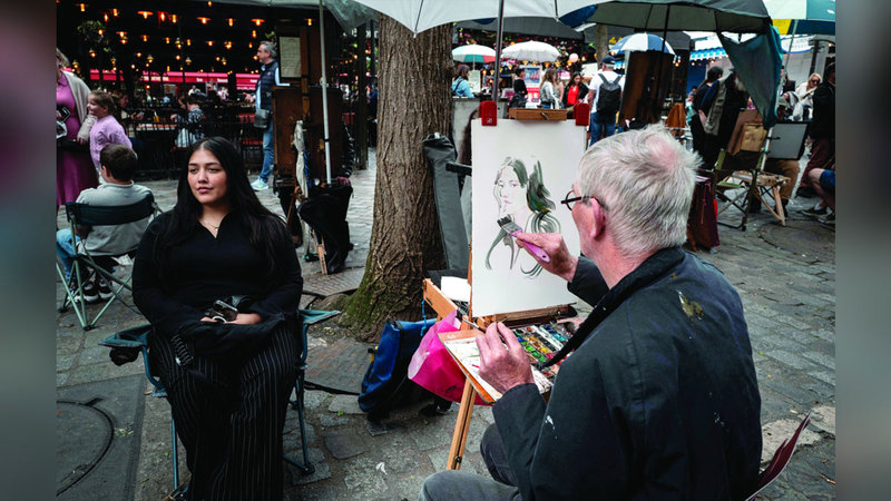 A woman poses for a portrait of a painter at Place du Tertre, the famous painters' square on the hill in the Montmartre district, northern Paris, on May 21, 2024. On the Place du Tertre, artists but there is no rush of tourists and the restaurant terraces are rather empty, just a few days before the 2024 Paris Olympics Games. (Photo by Miguel MEDINA / AFP)